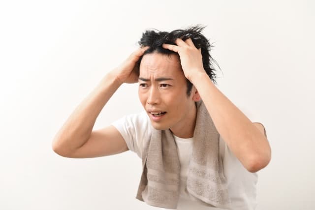 洗面所の鏡の前で前髪を上げて、生え際の後退を深刻な表情でチェックする男性